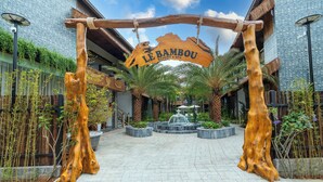 Ein hölzerner Bogen mit dem Schild "Le Bambou Resort & Spa" vor einem Gebäude mit einem Ziegeldach und Palmen.