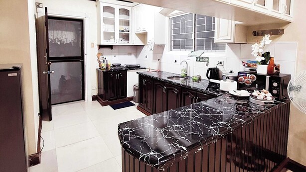 A modern kitchen with dark wooden cabinets, white upper cabinets, and a black marble countertop. - EA1 Studio Apartment Room near SM City Davao Costal Road & Ecoland Bus Terminal (Davao City)