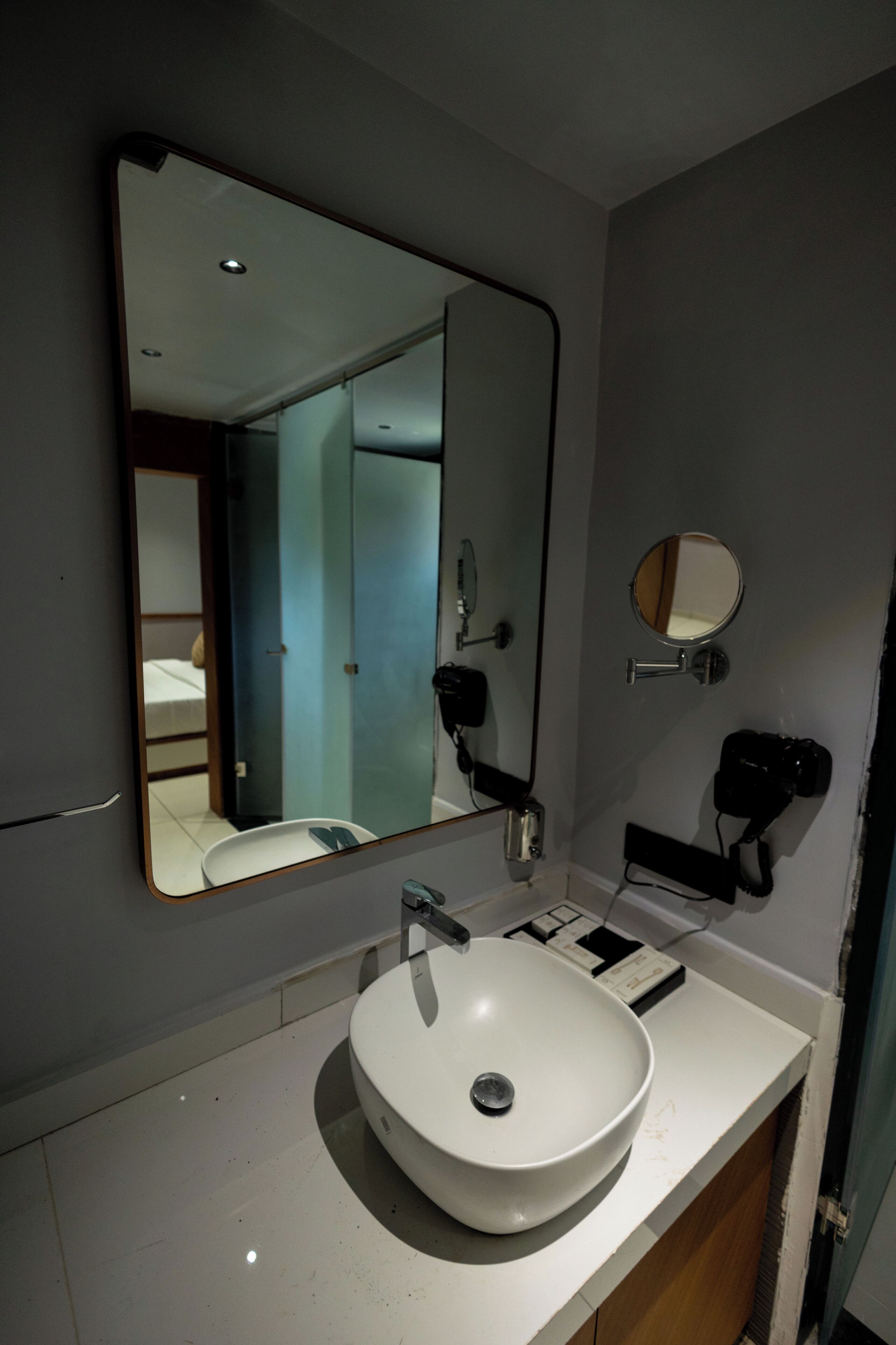 A modern bathroom with a white sink, a large mirror, and a handheld mirror.