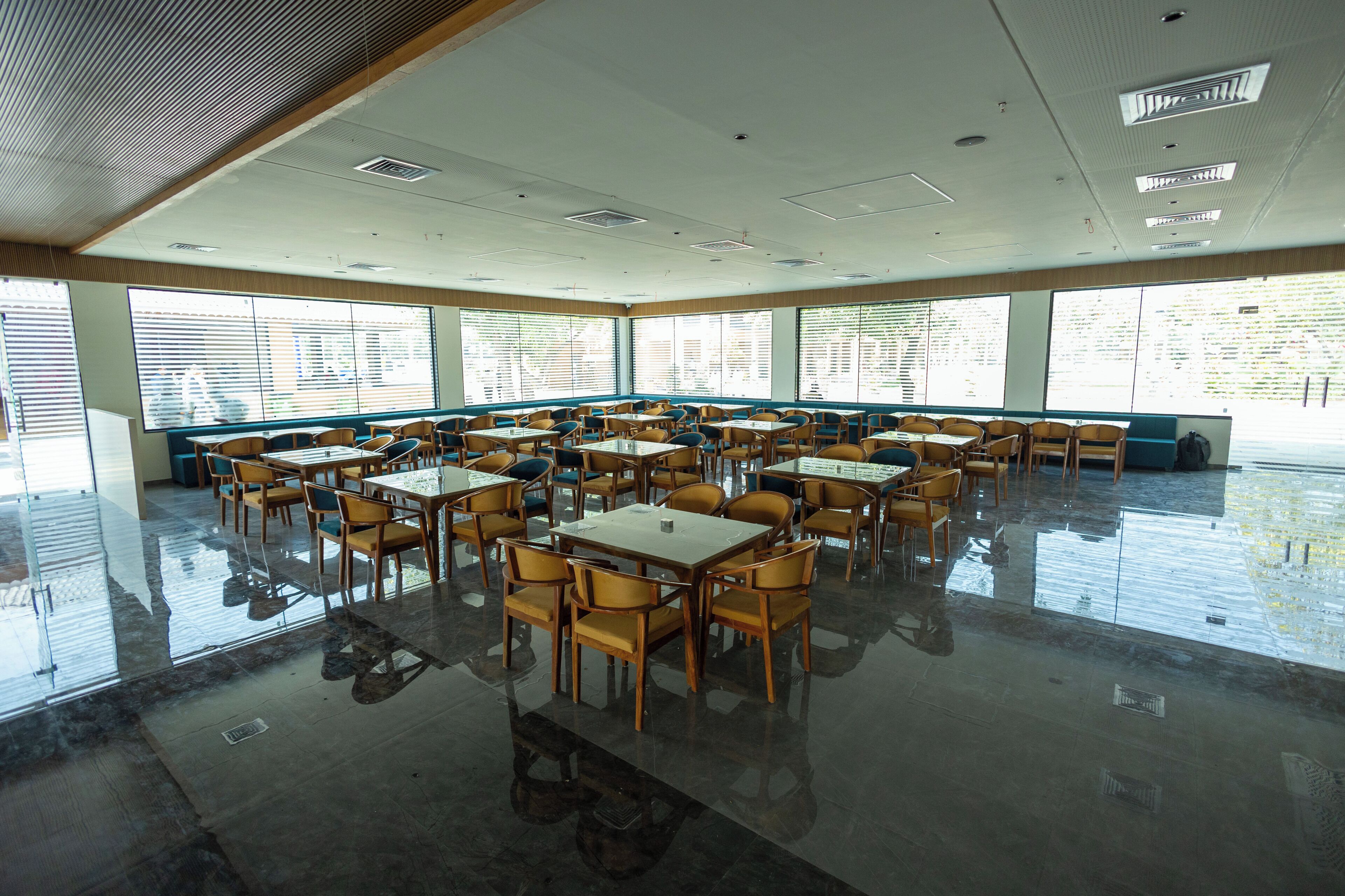 A spacious dining area with multiple tables and chairs, large windows, and a high ceiling with recessed lighting.