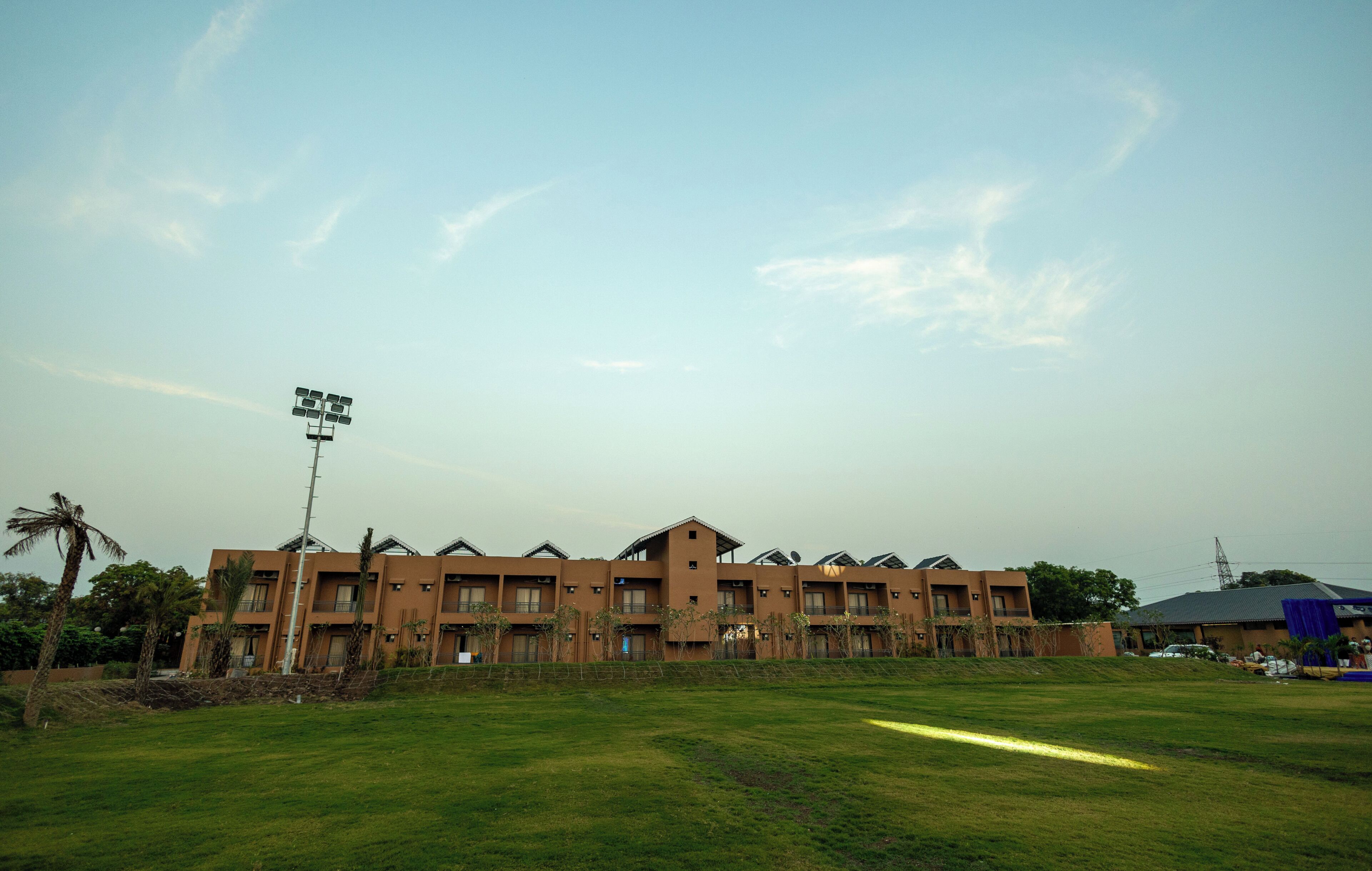 A multi-story building with a flat roof and a large open grassy area in front.