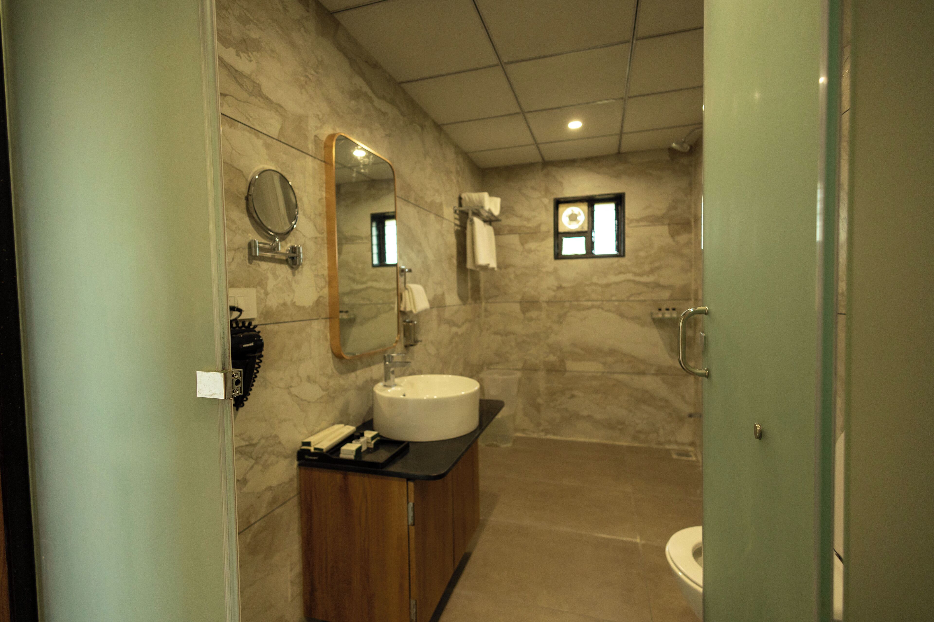 Un baño moderno con pared de mármol, un espejo redondo, un lavamanos y un inodoro.