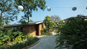 A pathway leading to a building with a tiled roof, surrounded by lush greenery and hanging spherical lights. - Madhuvan Resort (Talala)