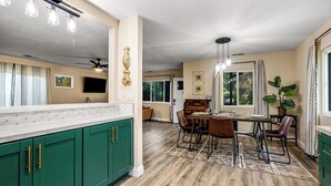 A spacious kitchen with green cabinets, a dining area with a wooden table and chairs, and a large window with curtains. - Buckthorn Beauty: Private Hot Tub & Lounge Space (Pine Valley)