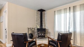 A living room with a fireplace, two leather chairs, a small round table, and patterned curtains. - Buckthorn Beauty: Private Hot Tub & Lounge Space (Pine Valley)