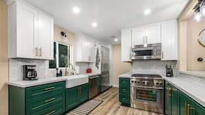 A modern kitchen with white cabinets, green drawers, stainless steel appliances, and a wooden floor. - Buckthorn Beauty: Private Hot Tub & Lounge Space (Pine Valley)