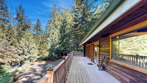 Une terrasse en bois mène à un chalet doté d’une porte en verre, le tout étant entouré d’une forêt dense.