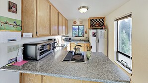 A kitchen with wooden cabinets, a microwave, a toaster, a kettle, and a window with a view.