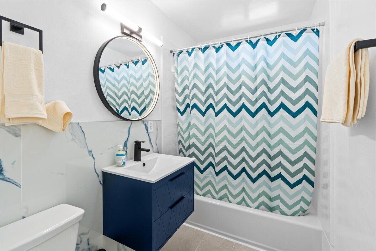 Casa de banho com sanita branca, toucador azul, espelho e cortina de chuveiro com padrão em chevron.