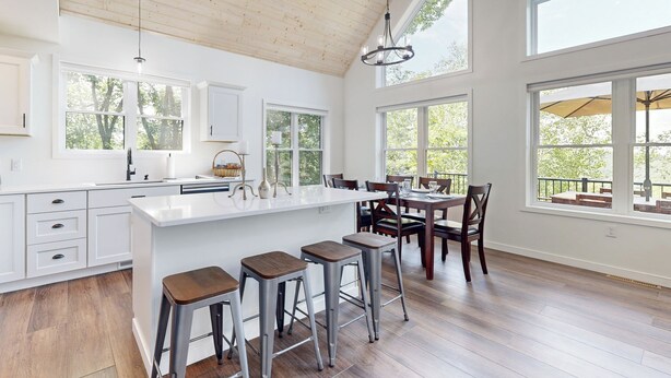 A spacious kitchen with a large island, wooden flooring, and large windows offering views of the outdoors. - Hot Tub, River Views! Luxurious Wisconsin Retreat (Eastman)