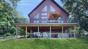 A two-story house with a balcony, large windows, and a covered outdoor area. - Hot Tub, River Views! Luxurious Wisconsin Retreat (Eastman)
