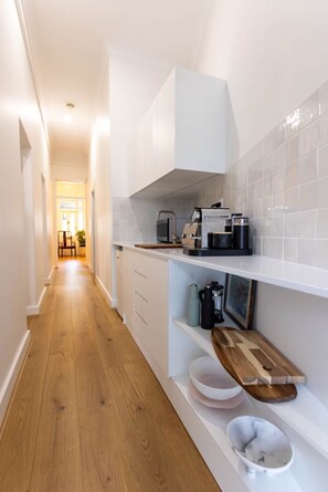 A narrow kitchen with white cabinets, a wooden countertop, and a coffee machine. - 1890s Sandstone Villa in Heart of Adelaide (Kent Town)
