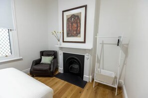 A bedroom with a fireplace, a bed, a chair, and a coat rack. - 1890s Sandstone Villa in Heart of Adelaide (Kent Town)