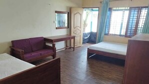 A room with a wooden floor, a purple sofa, a wooden bed, a wooden desk, and a wardrobe. - Shimana Periye Resort SaintMartin Island (Saint Martin's Island)