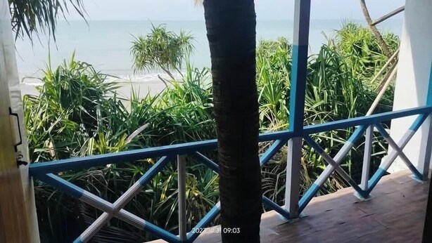 A covered outdoor area with a view of the beach, featuring a metal railing and tropical plants. - Shimana Periye Resort SaintMartin Island (Saint Martin's Island)