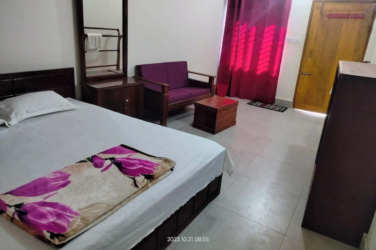 A hotel room with a bed, a chair, a small table, a mirror, a wardrobe, and a door.