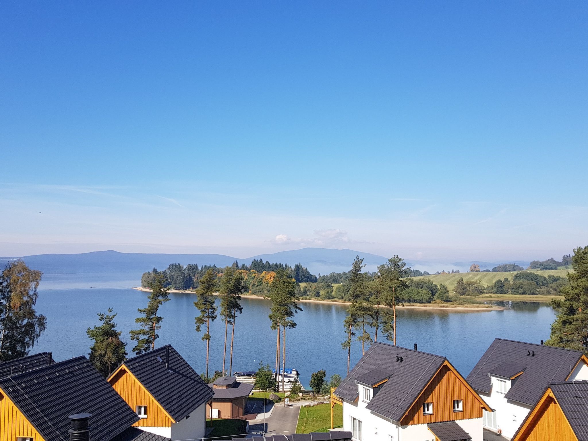 A lakeside view of a residential area with wooden houses, a clear sky, and distant mountains.