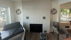 Un salon avec une cheminée en briques blanches, deux éléments décoratifs muraux, un canapé, un fauteuil et une petite table.