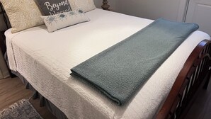 Un lit bien fait, recouvert d’une couette blanche, d’un plaid gris et agrémenté de deux coussins décoratifs à motifs floraux.