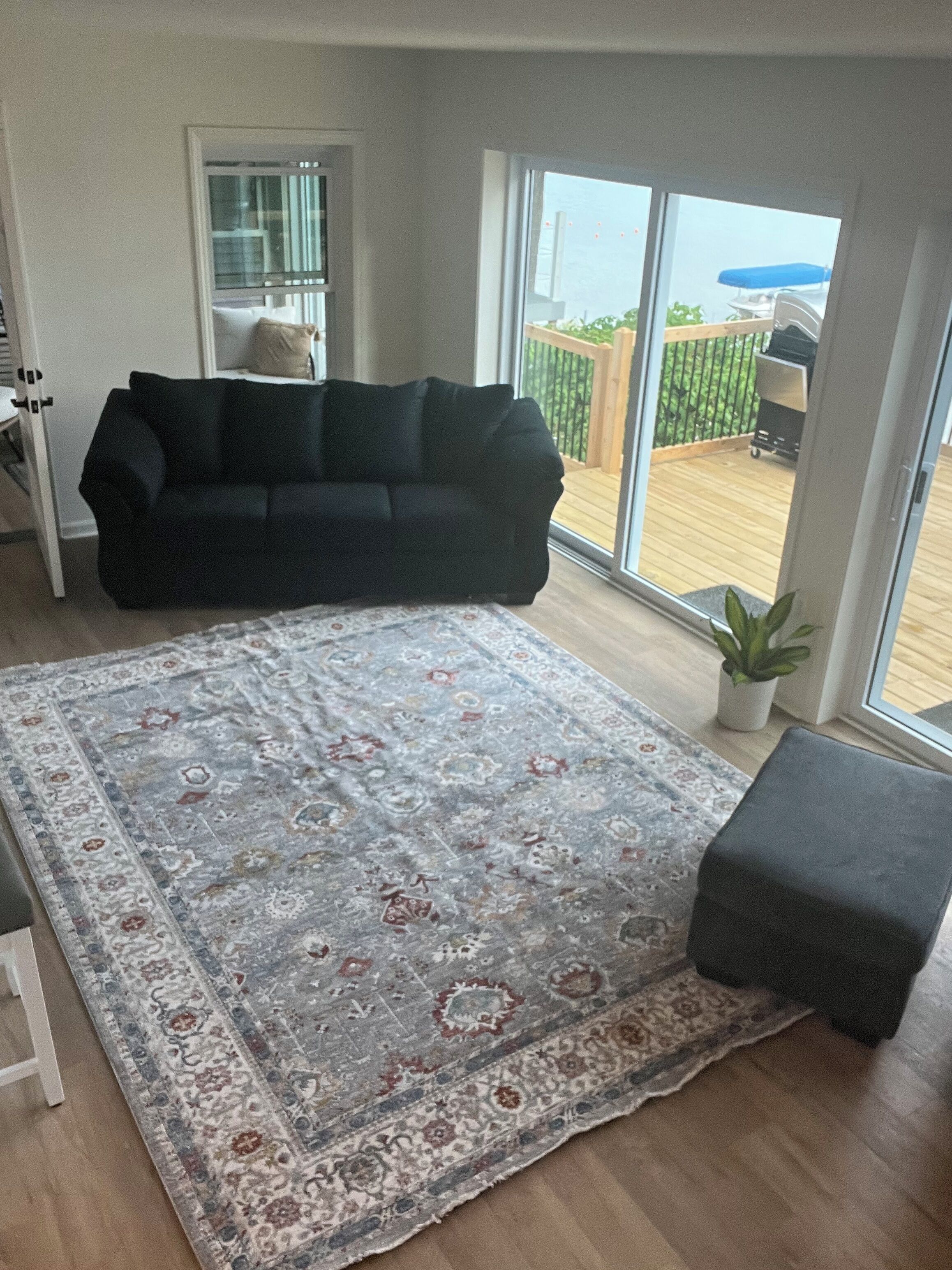 Een woonkamer met een zwarte bank, een kamerbreed tapijt en een houten terras zichtbaar door de glazen deur.