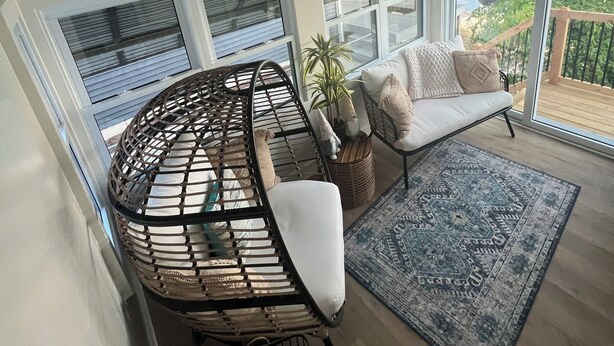 Un salon moderne avec un canapé aux lignes courbes, une petite table d’appoint, une plante en pot et une vue sur la mer grâce à de grandes fenêtres.