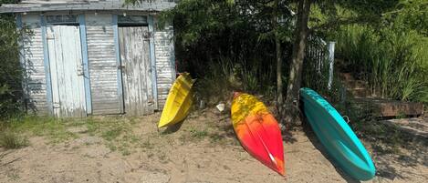 A sandy area with three kayaks and a small wooden shed.