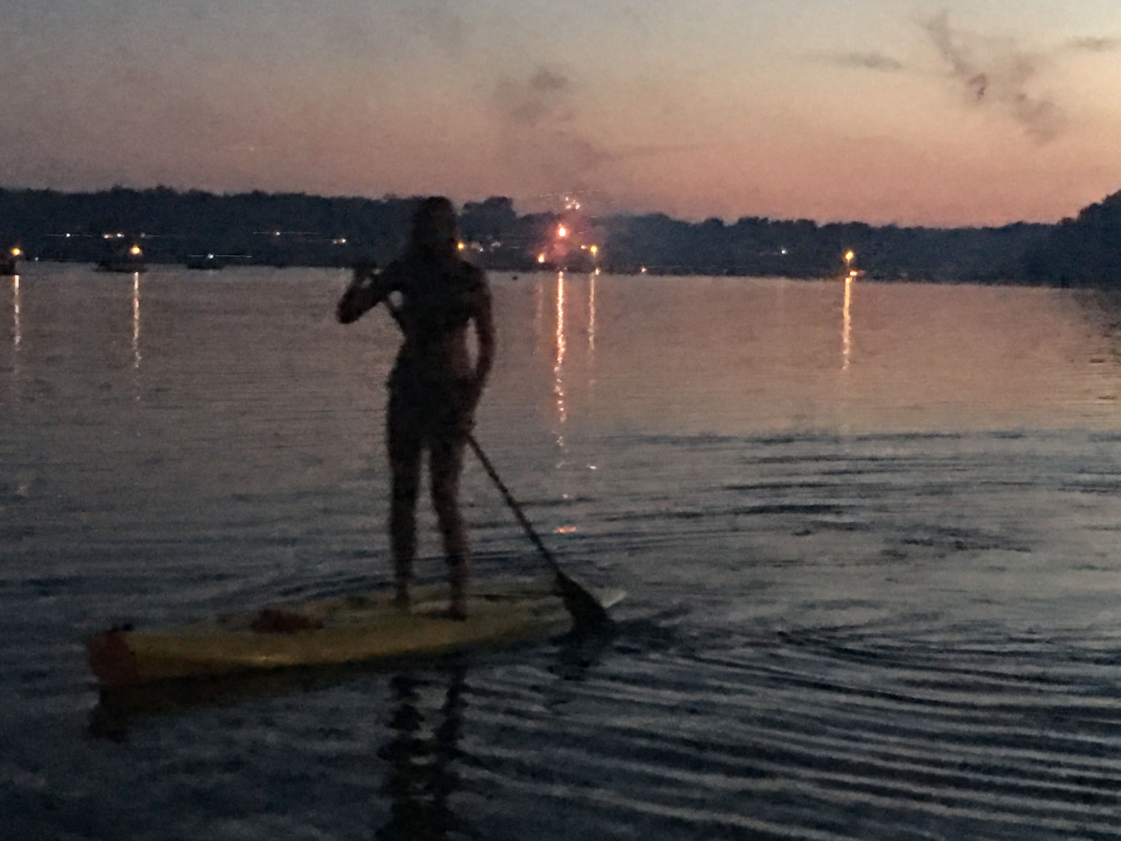 Eine Person steht auf einem Paddleboard auf ruhigem Wasser bei Dämmerung.
