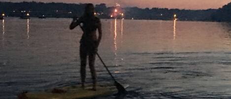 Eine Person steht auf einem Paddleboard auf ruhigem Wasser bei Dämmerung.