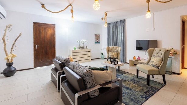 Una sala de estar moderna con sofá, sillón y mesa de centro, que incluye un televisor y elementos decorativos.