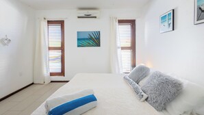 Un dormitorio con cama, dos ventanas con persianas, aire acondicionado de pared y un cuadro enmarcado.
