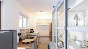 Una cocina compacta con refrigerador, lavamanos y una vitrina de vidrio que contiene vajilla.