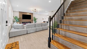 Ein modernes Wohnzimmer mit einem grauen Ecksofa, einer Holztreppe und einem flachbildfernseher an der Wand.