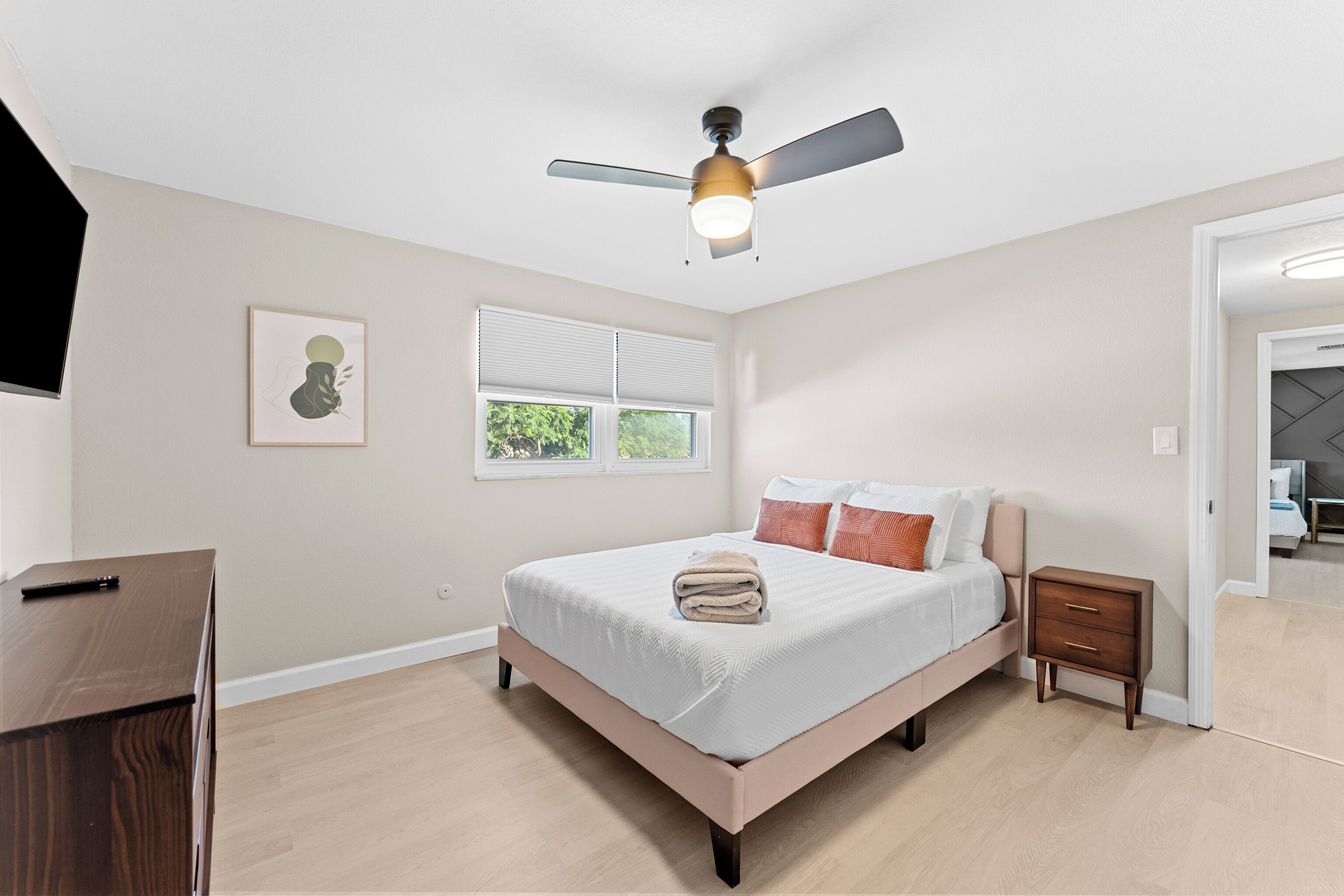 A bedroom with a bed, bedside tables, a ceiling fan, a window, and a door.