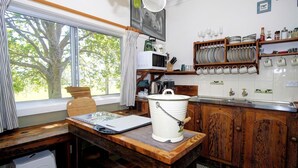 A kitchen with a wooden table, a white bucket, and a window with a view of trees. - Ashmar offers  you a  true country lifestyle.. (Gloucester)