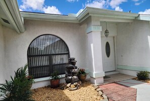 Una casa con un amplio ventanal de arco, una puerta principal y un pequeño elemento decorativo de agua al aire libre.