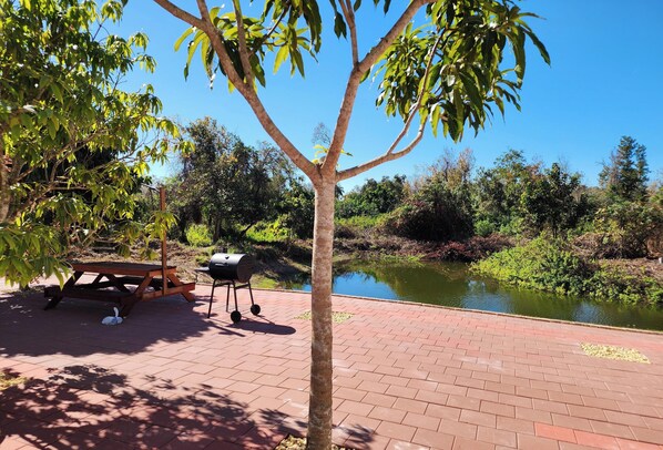 Una mesa de picnic y un juego de parrilla en un patio de ladrillo junto a un estanque.