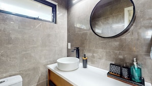 Un baño moderno con un espejo redondo, un lavabo blanco y un grifo negro.