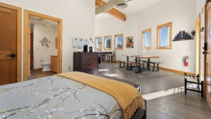 Een ruime slaapkamer met een groot bed, houten balken in het plafond, een bureau en een zithoek.
