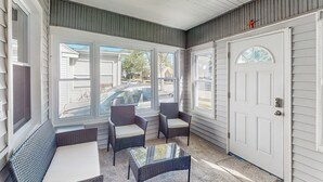 Une véranda avec des meubles en osier, une table en verre et une porte blanche.