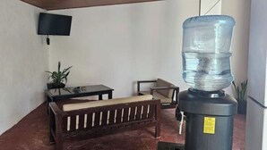 A room with a water dispenser, a TV mounted on the wall, a sofa, a small table, and a potted plant. - Casa Sol Managua: Your Warm and Familiar Refuge in Villa Sol (Managua)