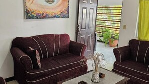 Un salon avec un canapé rouge foncé, un tableau représentant un œil accroché au mur et une porte donnant sur un balcon agrémenté de plantes.