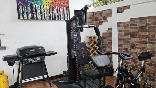 Une salle de sport à domicile équipée d’une machine Smith, d’un banc de développé couché et d’un vélo d’appartement.