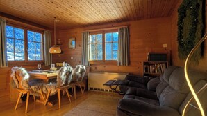 Interior acogedor de una cabaña con paredes de madera, un comedor con mesa y sillas, un sofá y una estantería.
