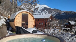 Una bañera de hidromasaje de madera en un entorno nevado al aire libre, con una montaña al fondo.