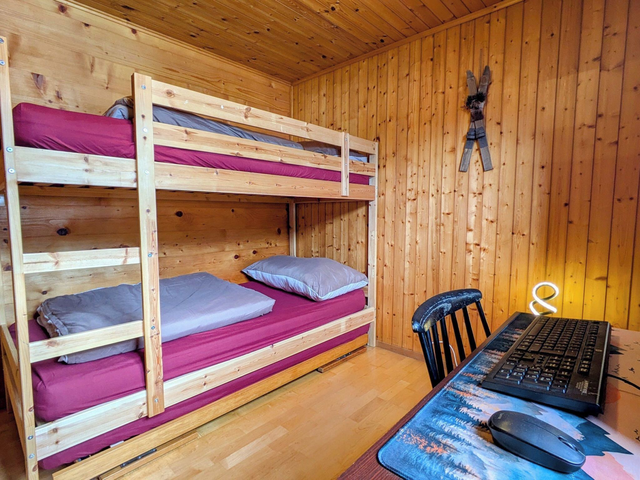 A bunk bed room with a wooden interior, a desk with a computer, and a chair.