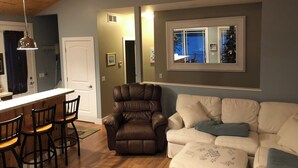 A living room with a brown leather chair, a white couch, and a wooden dining table with chairs. - Eagles Landing - Lakefront Home on crystal clear Wolf Lake (Muskegon)
