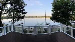 A wooden deck with a white railing overlooking a calm lake, surrounded by trees. - Eagles Landing - Lakefront Home on crystal clear Wolf Lake (Muskegon)