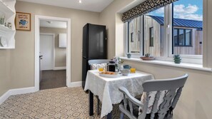 Un coin repas avec une table mise pour le petit-déjeuner, un réfrigérateur noir et une fenêtre donnant sur l’extérieur.