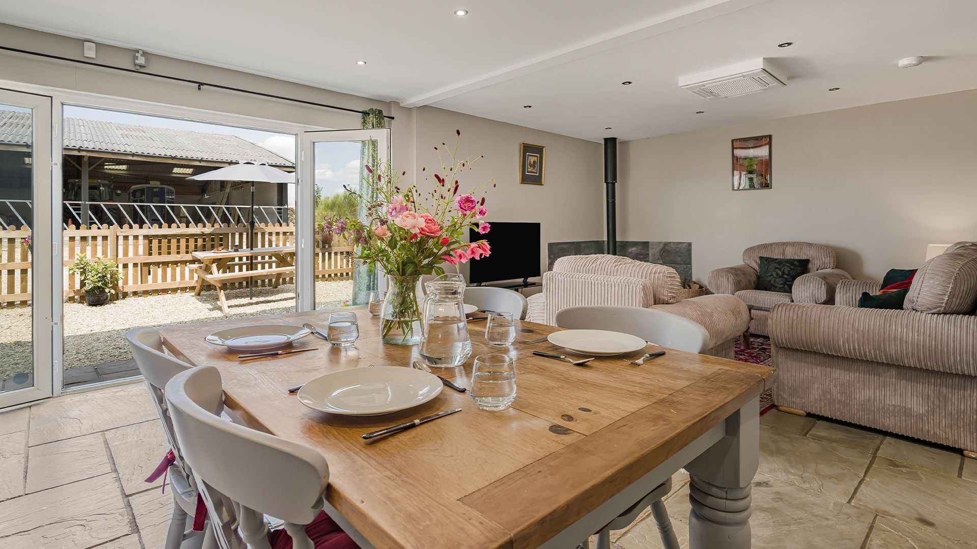A dining area with a wooden table set for four, a vase with flowers, and a view of the outdoor patio.