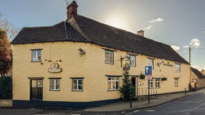 Un bâtiment jaune avec une enseigne indiquant « The Rattlebone Inn » et un panneau de signalisation indiquant la priorité de passage par rapport aux véhicules venant en sens inverse.